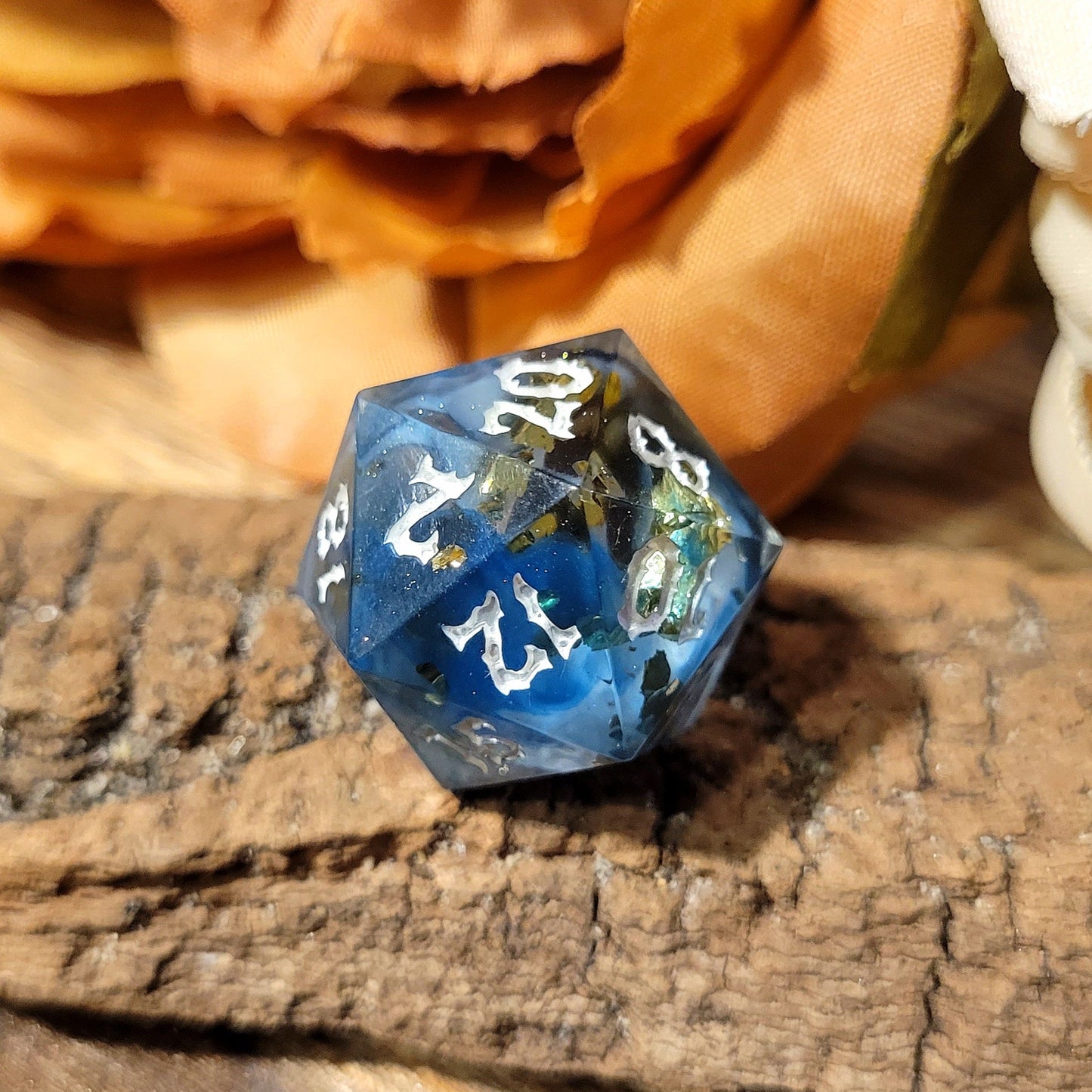 A twenty-sided die that has a clear base with black, white, and Oxford blue drips. The font is Sugar Bee RPG's signature death metal font, and is inked in white. The most prominent numbers are 20, 2, 18, 8, 12, and 10.