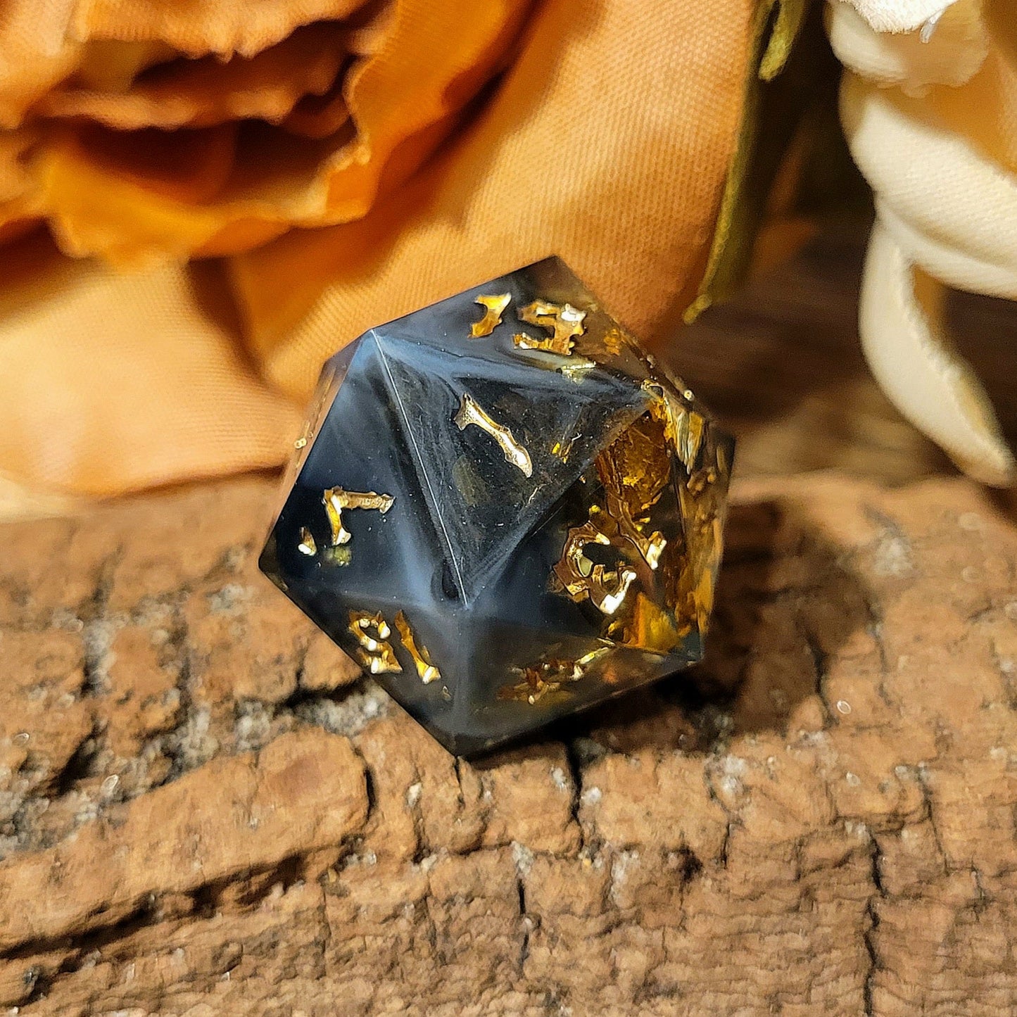 A twenty-sided die that has a clear base with black, white, and Oxford blue drips. The font is Sugar Bee RPG's signature death metal font, and is inked in gold. The most prominent numbers are 19, 1, 7, 15, and 13. Large gold foil flakes are suspended within the die. This angle looks inky and dark with splashes of milky blue.